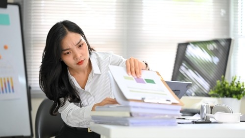 A focused businesswoman reviews financial data charts and paperwork at an office desk.