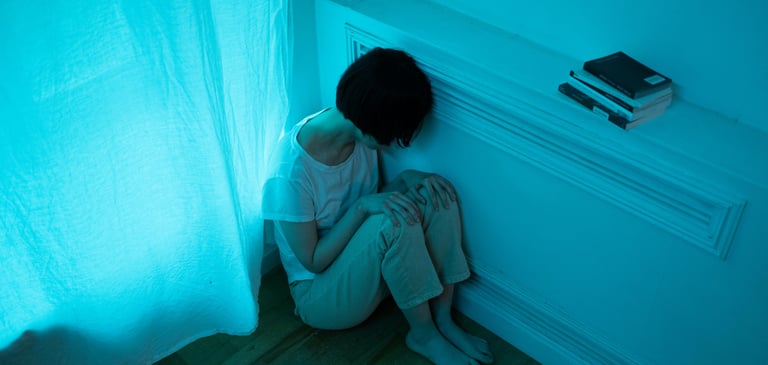 Pessoa sentada no chão da sala, demonstrando tristeza. 