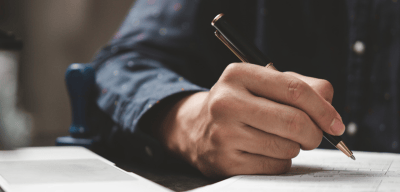 a man is writing on a notebook and holding a pen