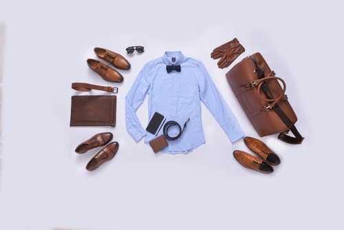 Flat lay of men's formal fashion accessories including a blue shirt, brown leather shoes, and a duffel bag.