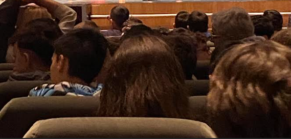 a man in a suit and tie is standing in front of a lecture hall