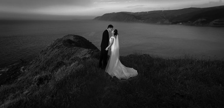 a bride and groom standing on a cliff overlooking the ocean