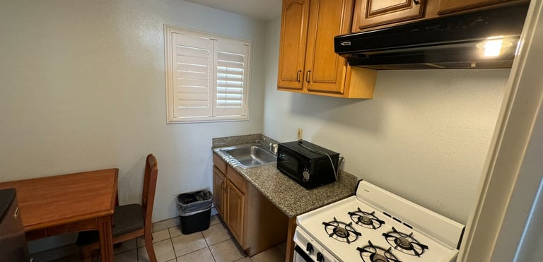 a kitchenette with a stove top oven, sink, microwave and table with a chair