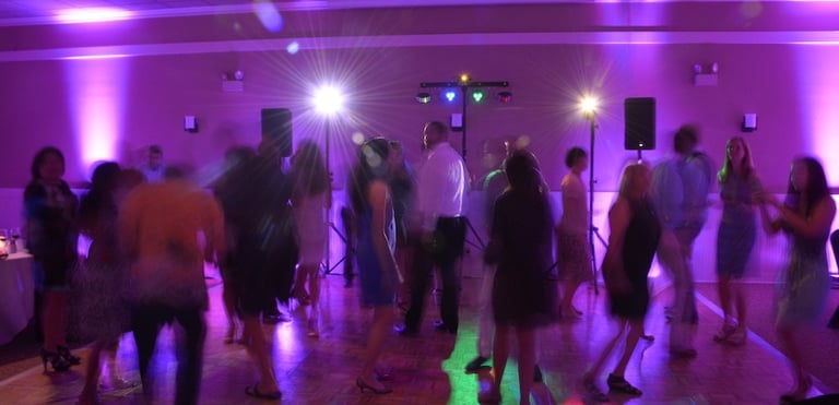 Wedding guests dancing on a wooden dance floor with purple uplighting and disco stage lights.