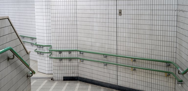 Subway station ramp with white tiles, green metal handrails, and yellow tactile paving for accessibility.