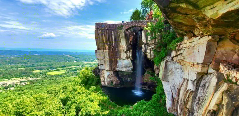 Lookout Mtn, GA - A view looking up at a stone footbridge & waterfall at the clifftop of Rock City
