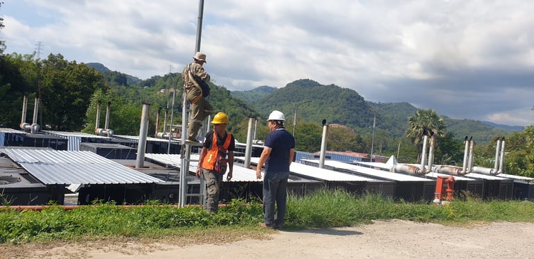 Engineers in hard hats inspecting an industrial power plant facility in a rural mountain landscape.