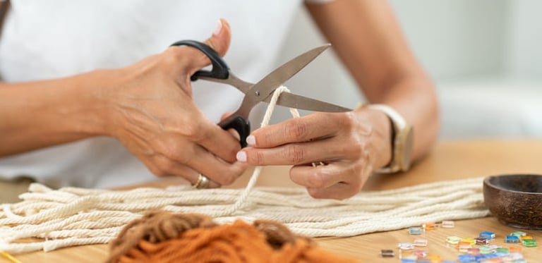 Mujer cortando materiales para hacer una pieza de macramé 