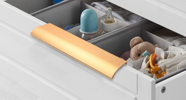 Gold flush cabinet handle on a baby nursery drawer – sleek hardware for organized nursery storage.