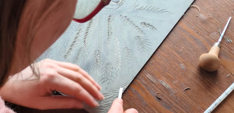 Artist carving an intricate botanical linocut print on a grey lino block using professional gouge tools.