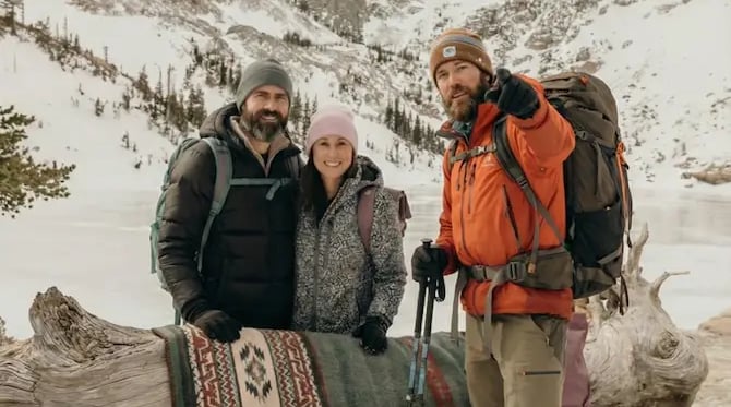Three hikers posing with a colorful blanket at frozen Emerald Lake in winter.