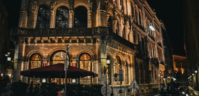 The historic Palais Ferstel building in Vienna illuminated at night with a street cafe and horse-drawn carriage.