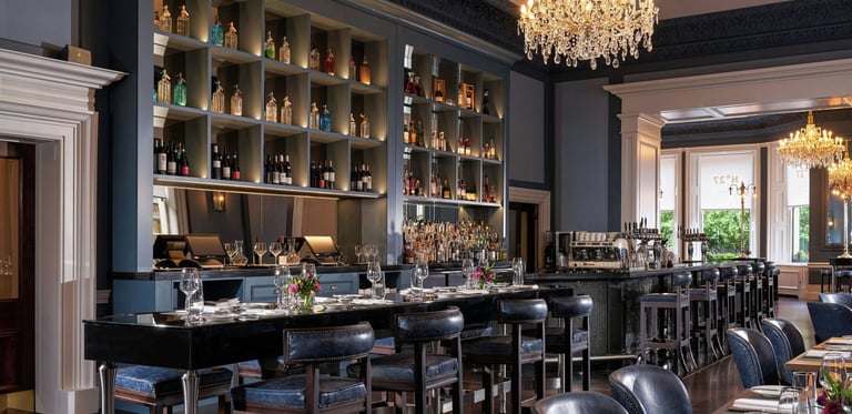 Elegant luxury bar and restaurant interior featuring leather stools, crystal chandeliers, and a backlit liquor shelf.