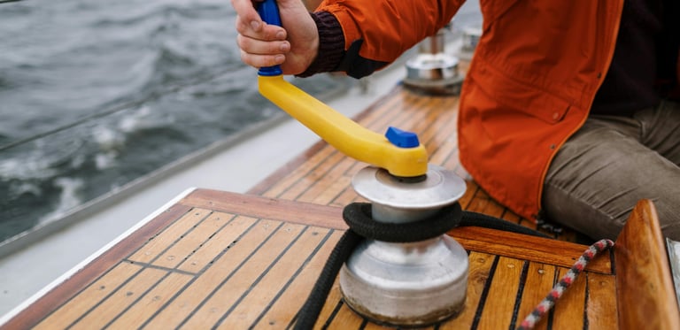 a man in a red jacket is holding a winch on a sailing boat