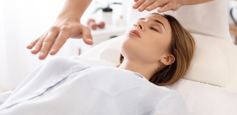 Sesión de Reiki en una camilla de terapeuta, vemos a una mujer joven recibiendo energía reiki del terapeuta, en parte superio