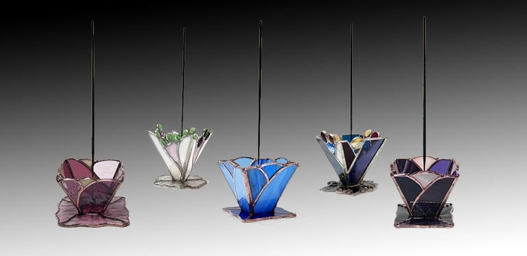 A collection of five stained glass incense holders in various floral shapes and vibrant colors, each with an incense stick