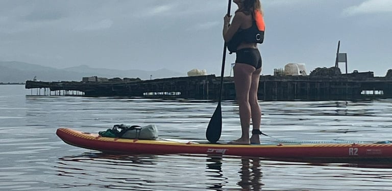 Chica sobre una tabla de paddel surf junto a una batea mientras hace el camino de santiago