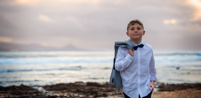 a young boy in a white shirt and tie dye on a beach