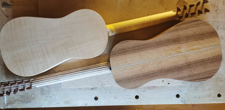 Two handmade baroque guitars in progress showing flamed maple and walnut wood grain on a workbench.