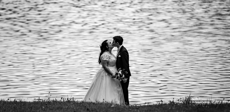 a bride and groom kissing in front of a lake