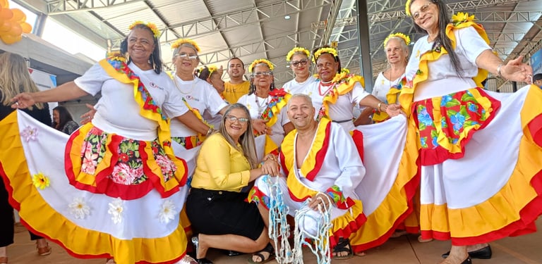 Seniors in colorful traditional folk costumes performing a cultural dance at an indoor community festival.