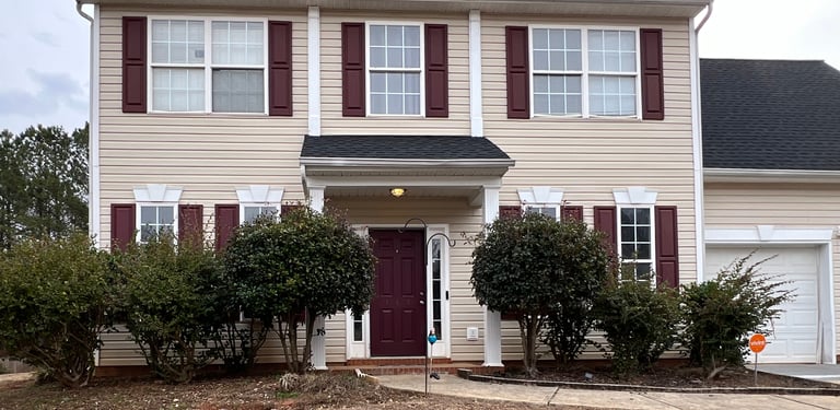 Front of a house with overgrown shrubs covering the windows.