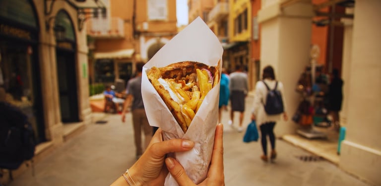 Autora segurando um gyros enquanto caminha pelas ruelas movimentadas de Corfu, explorando a cidade.