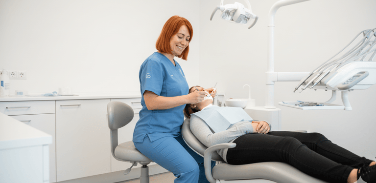 Una dentista sonriente realizando un examen dental a una paciente recostada en el sillón dental