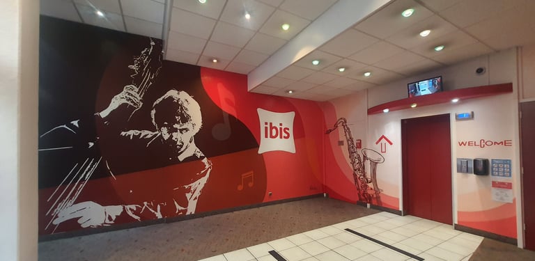 Modern ibis hotel lobby featuring red jazz-themed wall murals, a double bass player, and elevators.