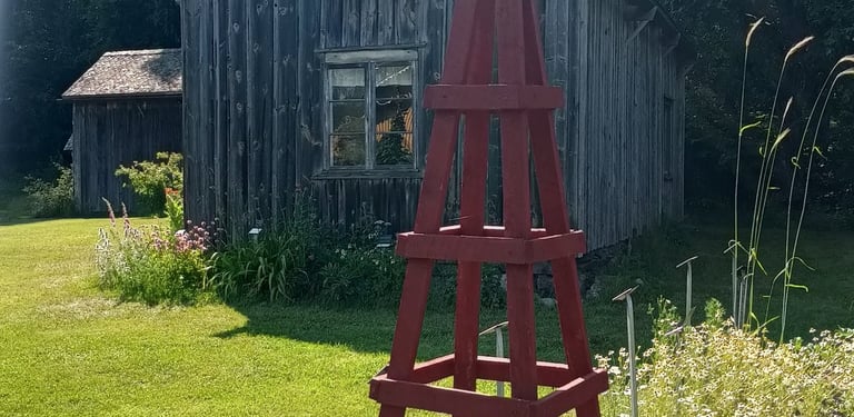 un tuteur de jardin peint en peinture naturelle suédoise en forme pointue devant une vieille maison en bois