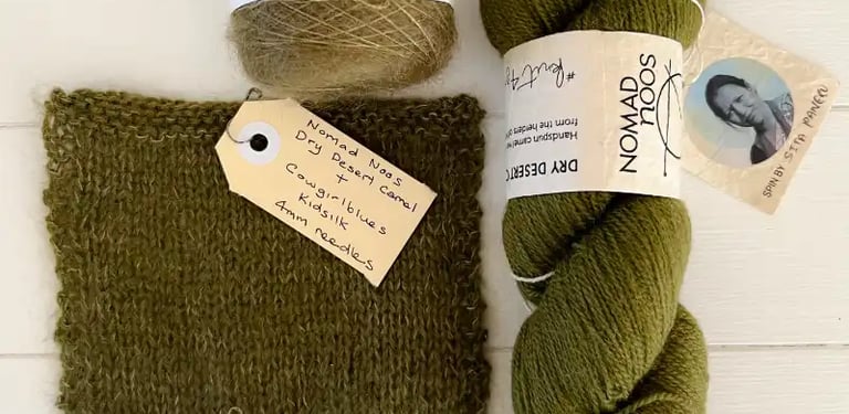 Green yarns and a square of knitting on a white table at Paddock and Purl Studio