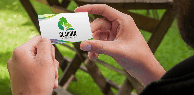Une personne tient une carte de visite de paysagiste avec un logo d'arbre vert à l'extérieur.