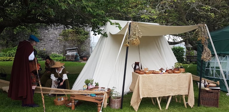 reenactors talking beside a medieval tent with a table of herbal remedies