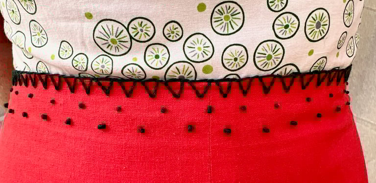 Embroidered waist of a white, green, and red strappy sundress