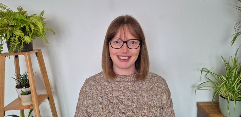 A smiling woman sits between leafy green plants