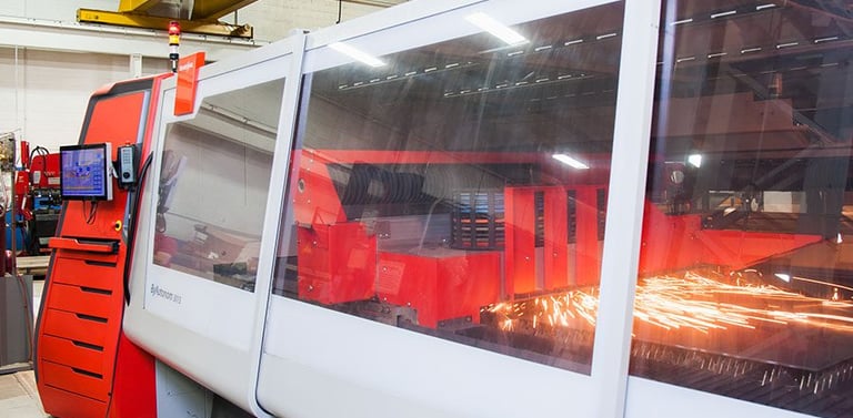 Industrial CNC laser cutting machine in a factory workshop creating sparks during metal fabrication.