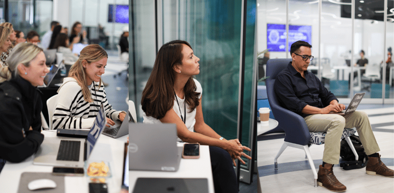 a group of people sitting at a table with laptops using AI to code