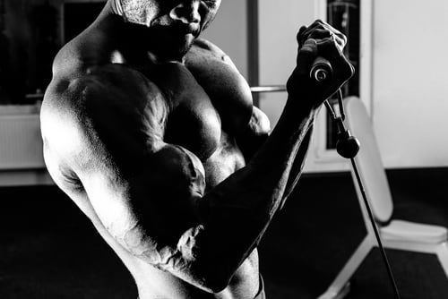 Black and white photo of a muscular bodybuilder performing cable bicep curls in a gym.