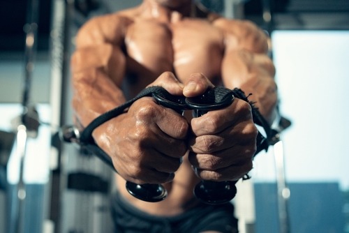 Muscular male bodybuilder performing a cable fly chest workout in a gym for muscle growth.