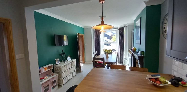 Open kitchen/dining room, with wood table, wood kitchen island, white ceiling, and emerald walls.