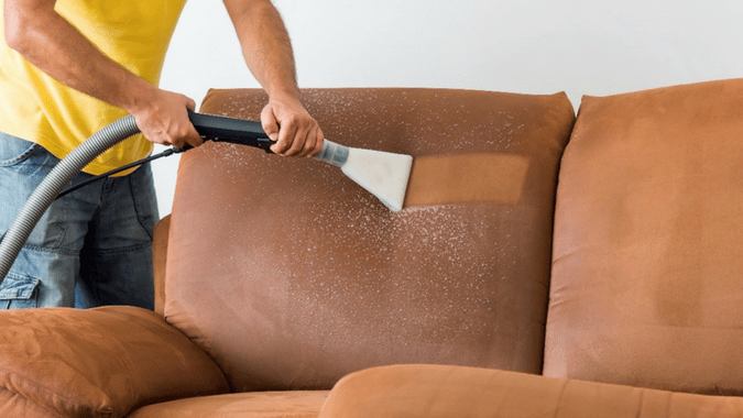 a man cleaning a couch with a vacuum cleaner