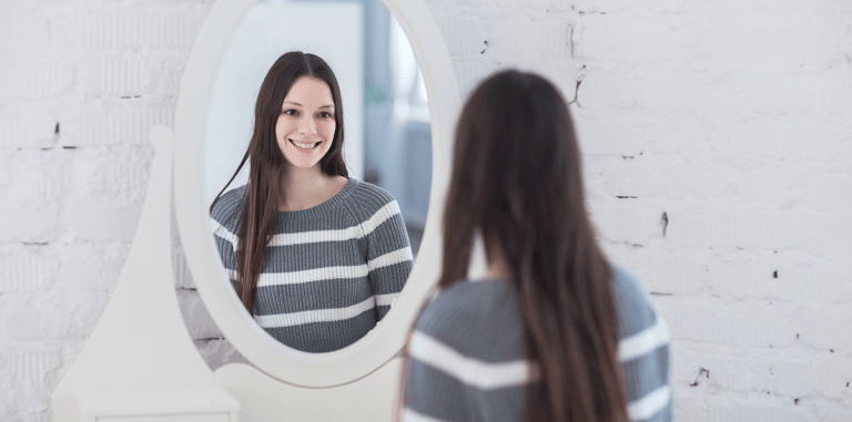 Mujer joven contemplándose al espejo. Se nota contenta consigo misma, buena autoestima.
