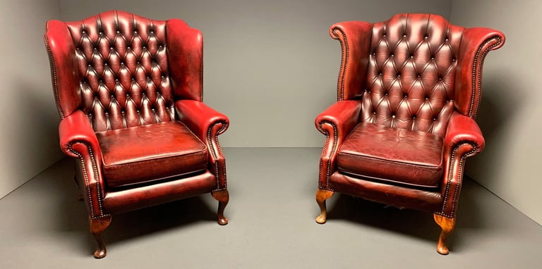 Two vintage, orang leather armchairs with tufted backs sit side by side in a minimalist, neutral-colored room. 