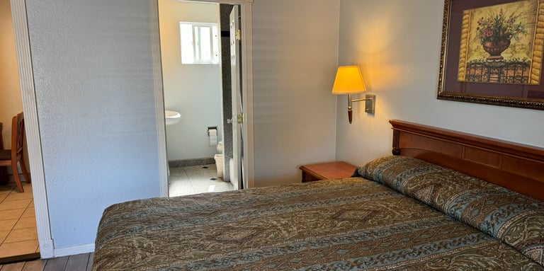 a motel room with a queen bed and a lamp with the bathroom in the background
