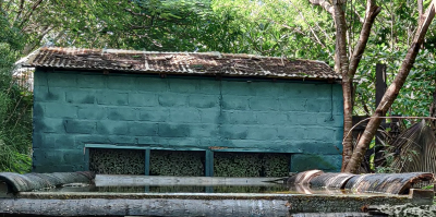 Een langwerpig groen stenen gebouw met een golfplaten dak,.