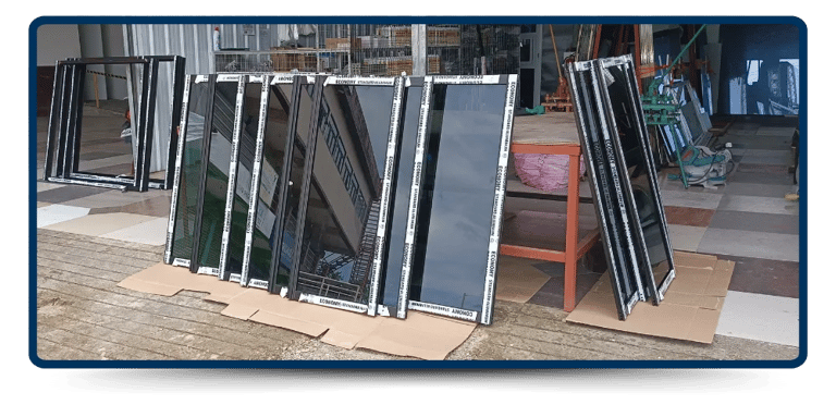 Several black-framed glass panels are neatly arranged on cardboard outside a workshop, with tools and materials