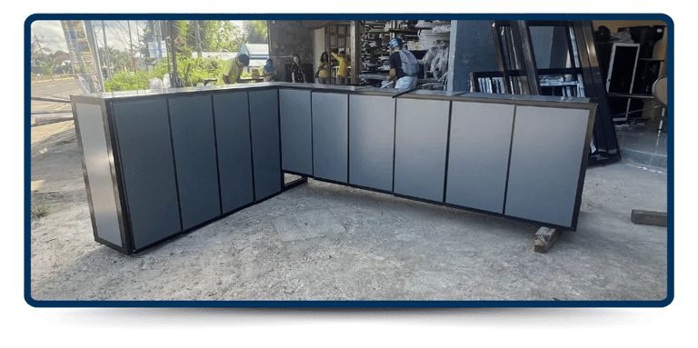 A sleek, modern gray aluminum cabinet is displayed outdoors, with construction materials visible in the background