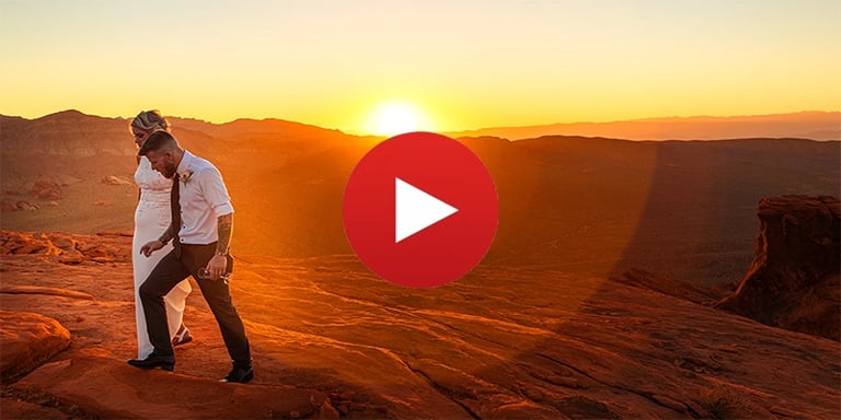 A bride and groom walk across red rock cliffs at sunset during their Las Vegas desert elopement.