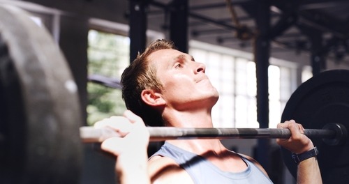 Focused athlete performing a barbell overhead shoulder press at a fitness gym.