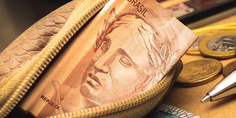imagem de uma bolsa pequena com dinheiro dentro e moedas ao fundo  de uma mesa 